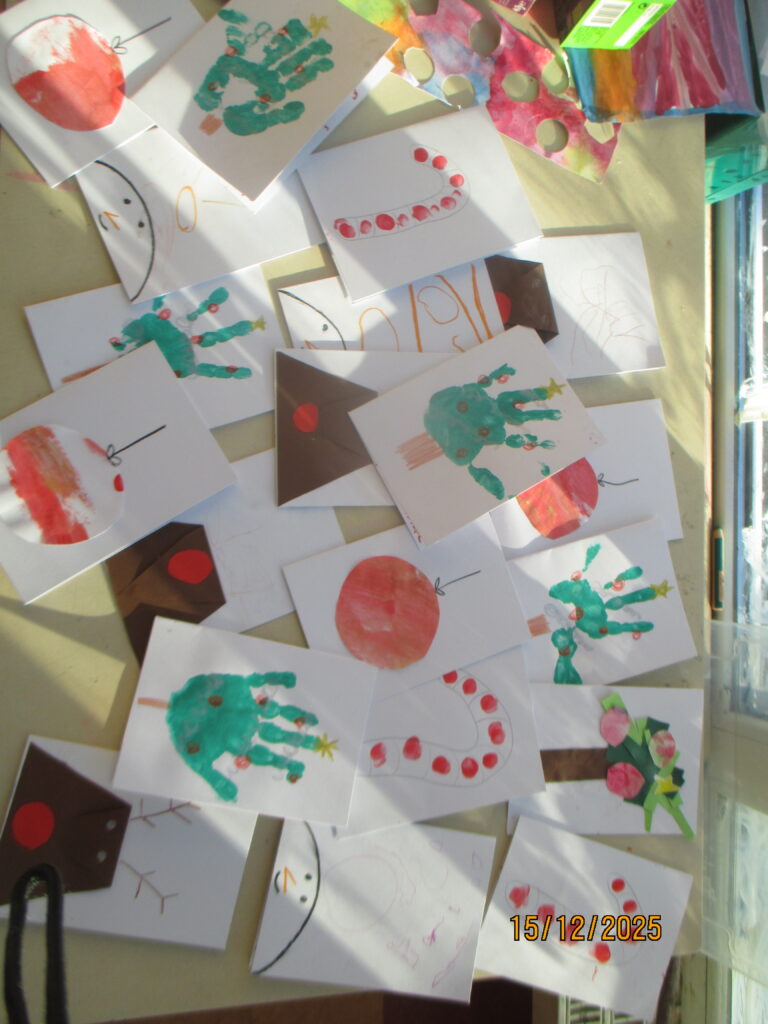 Viele unterschiedliche selbst gestaltete Weihnachtskarten der Kinder liegen ausgebreitet auf einem Tisch im Sonnenlicht.