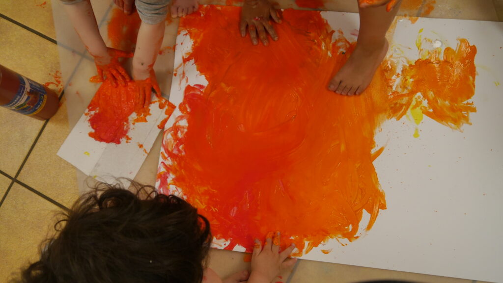 Kinder gestalten ein großes Feuerbild mit orangefarbenen Farbflächen auf Papier.